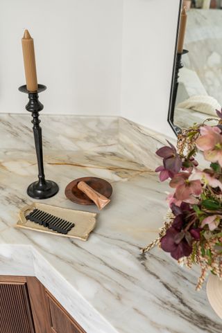 A marble vanity top close up of a candlestick, comb and product with some warm pink flowers to the side