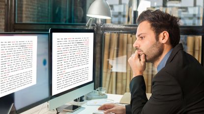 An editor looks at a pair of computer monitors and ponders.