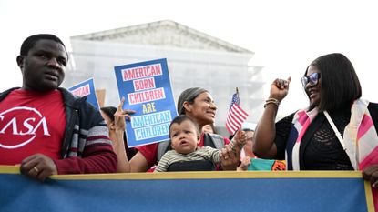 A woman holds her baby as a crowd gathers outside the Supreme Court in protests against Trump's policy to end birthright citizenship