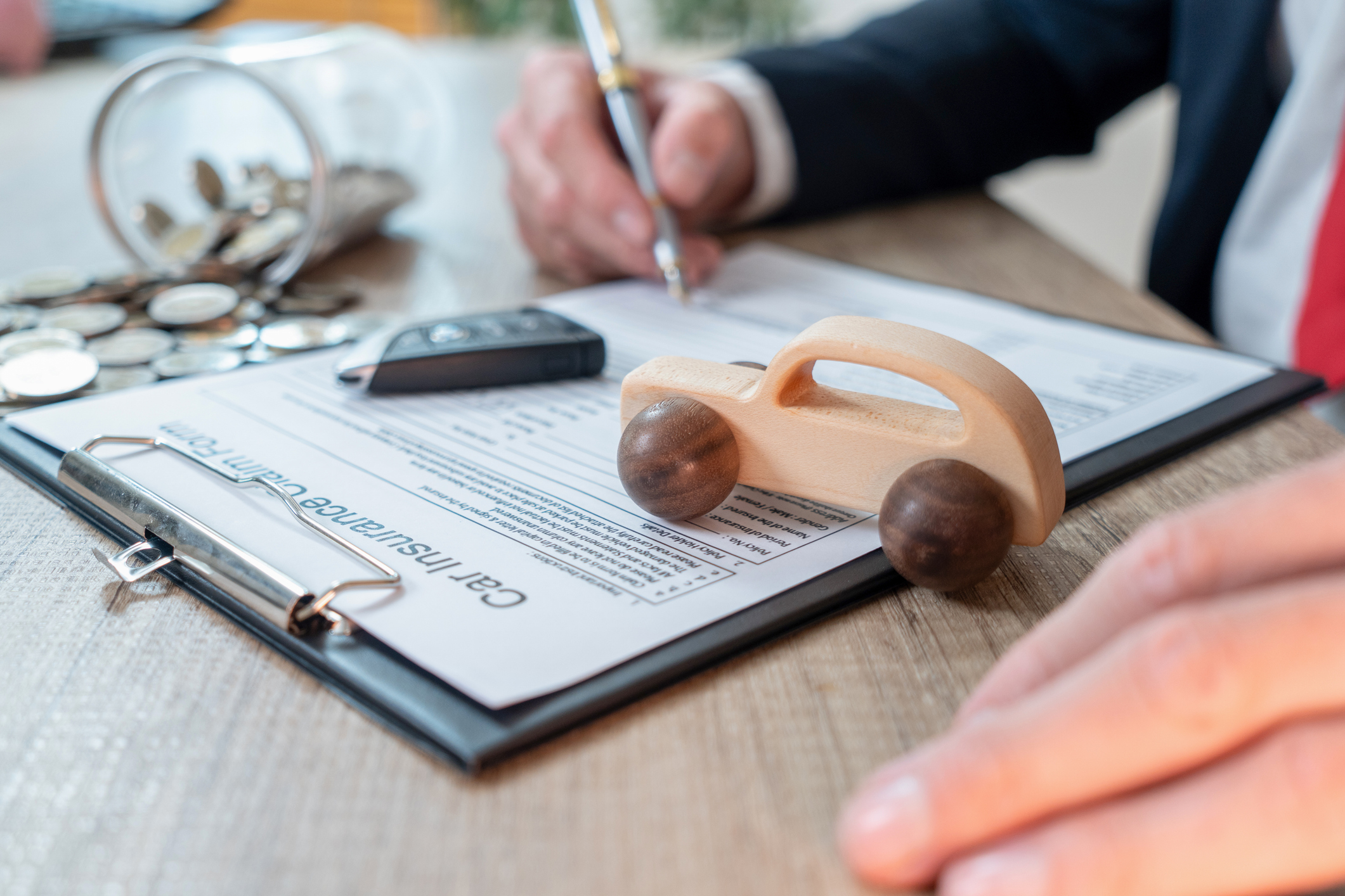Person filling out a car insurance form with a wooden car on the table