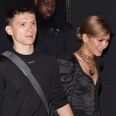 Tom Holland holds hands with fiancee Zendaya who wears a black dress