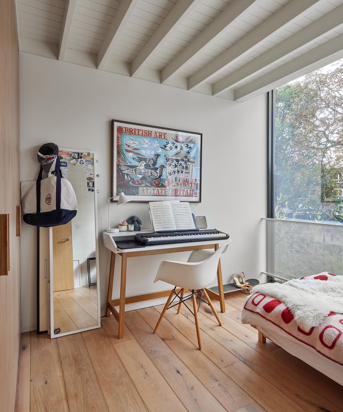 A musical keyboard set up in a teenagers bedroom with framed art on the walls and light wooden floorboards