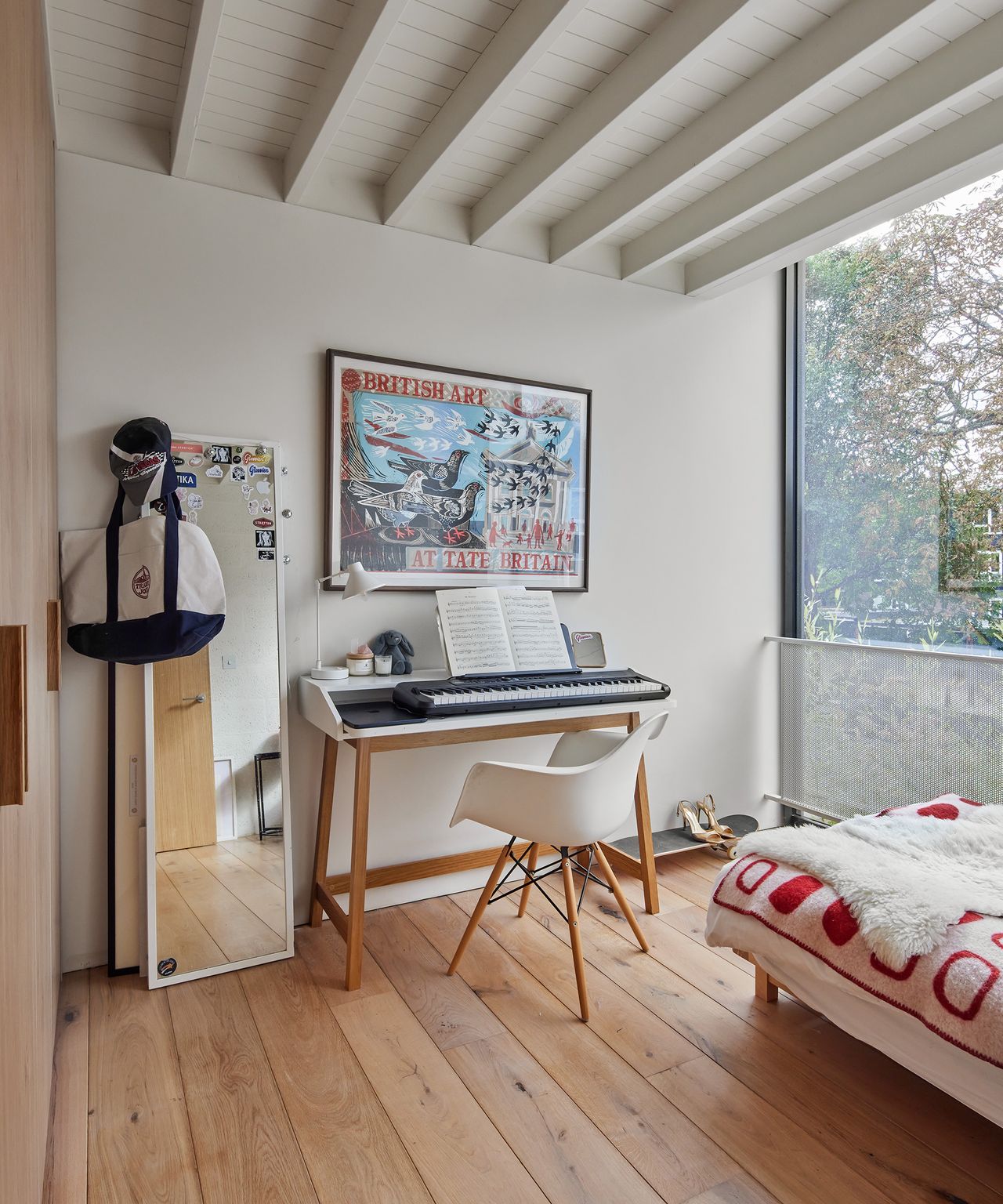 A musical keyboard set up in a teenagers bedroom with framed art on the walls and light wooden floorboards
