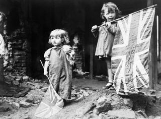 Two small girls waving their flags in the rubble of Battersea, snapped by an anonymous American photographer.