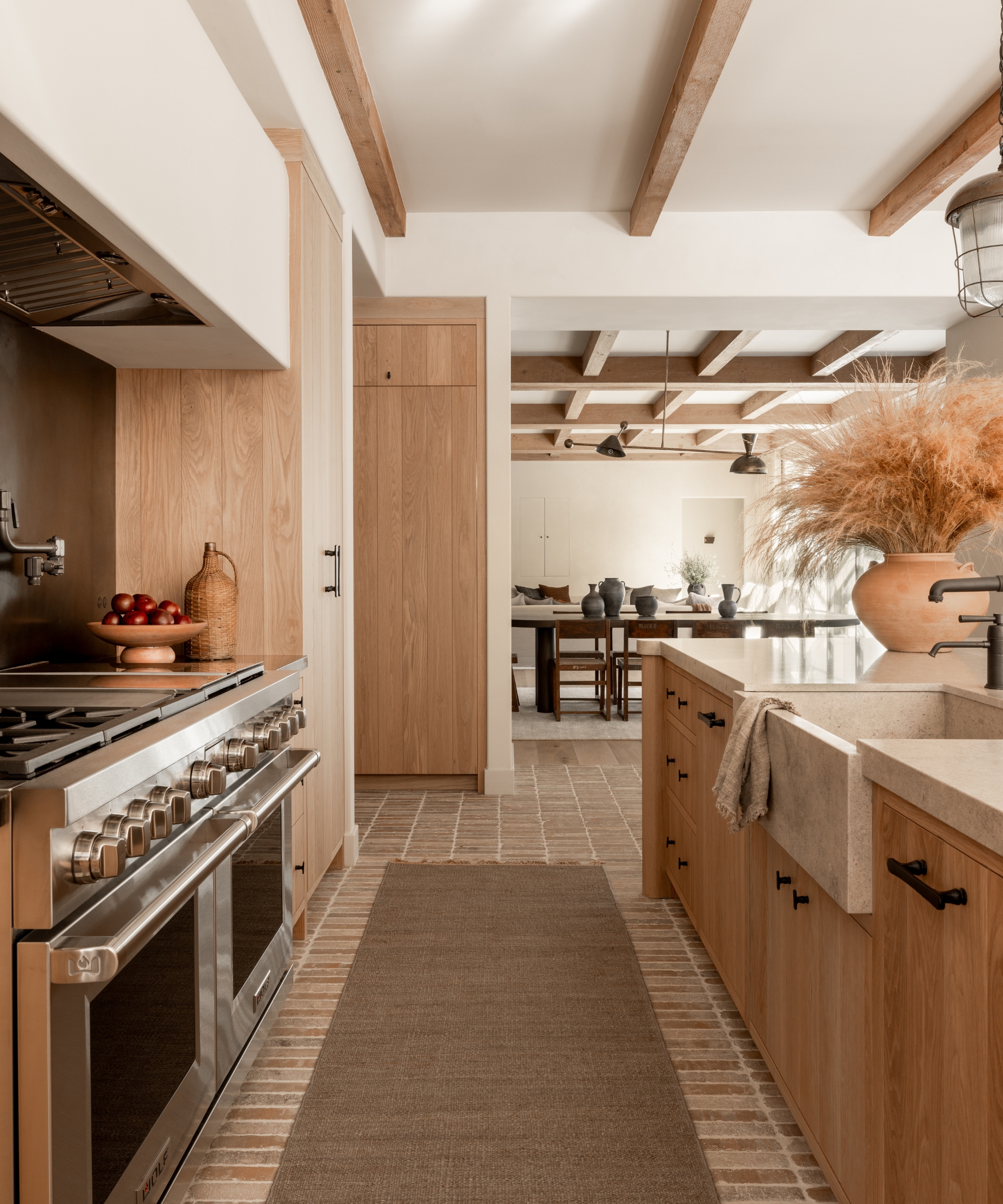 A wooden kitchen with brick flooring, a stainless steel range, and a natural hessian runner of the floor