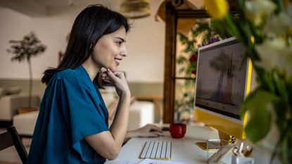 A young, smiling woman looks at her personal computer at home. She appears to be looking at investing or business data. 