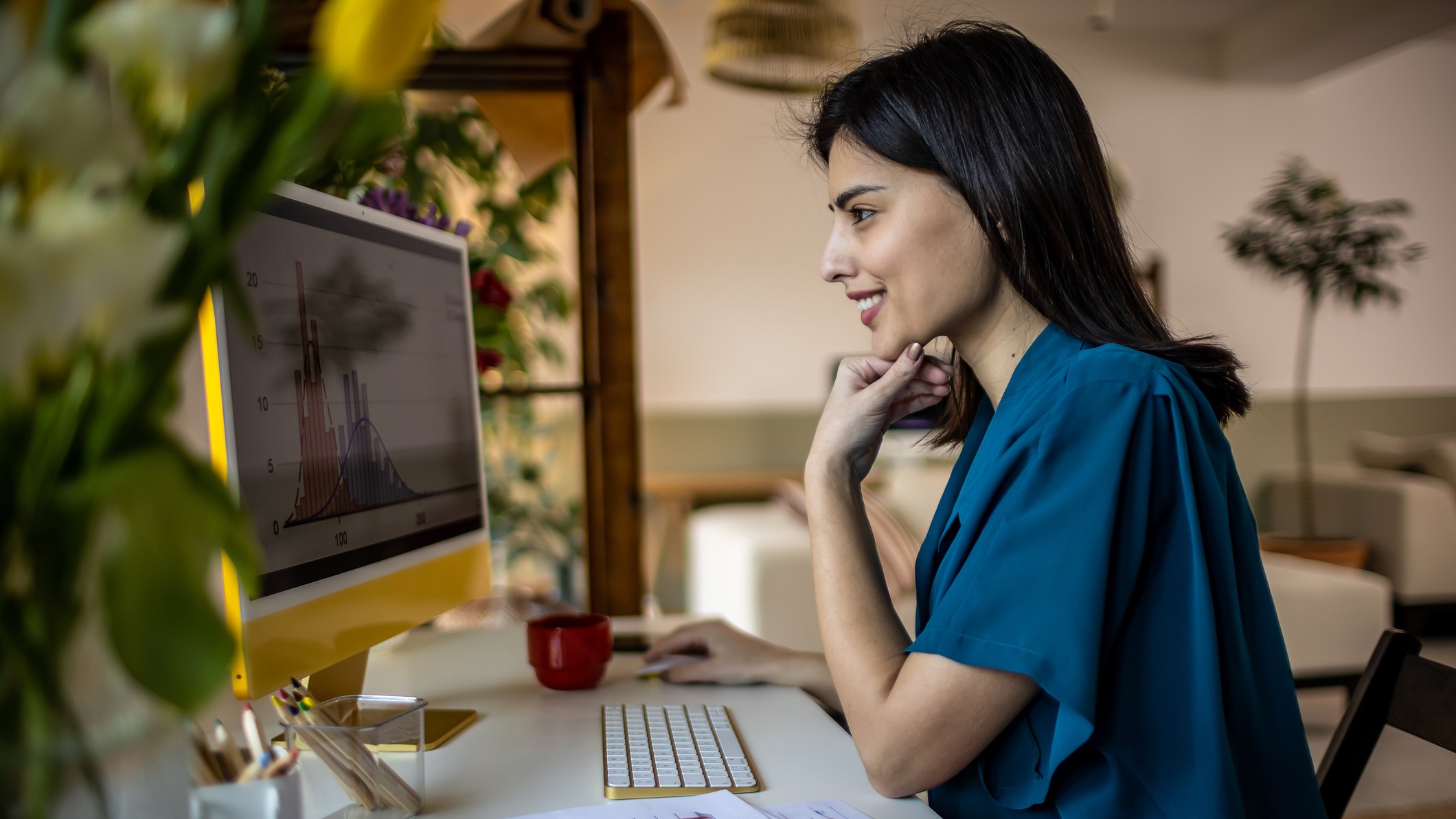 A young, smiling woman looks at her personal computer at home. She appears to be looking at investing or business data. 