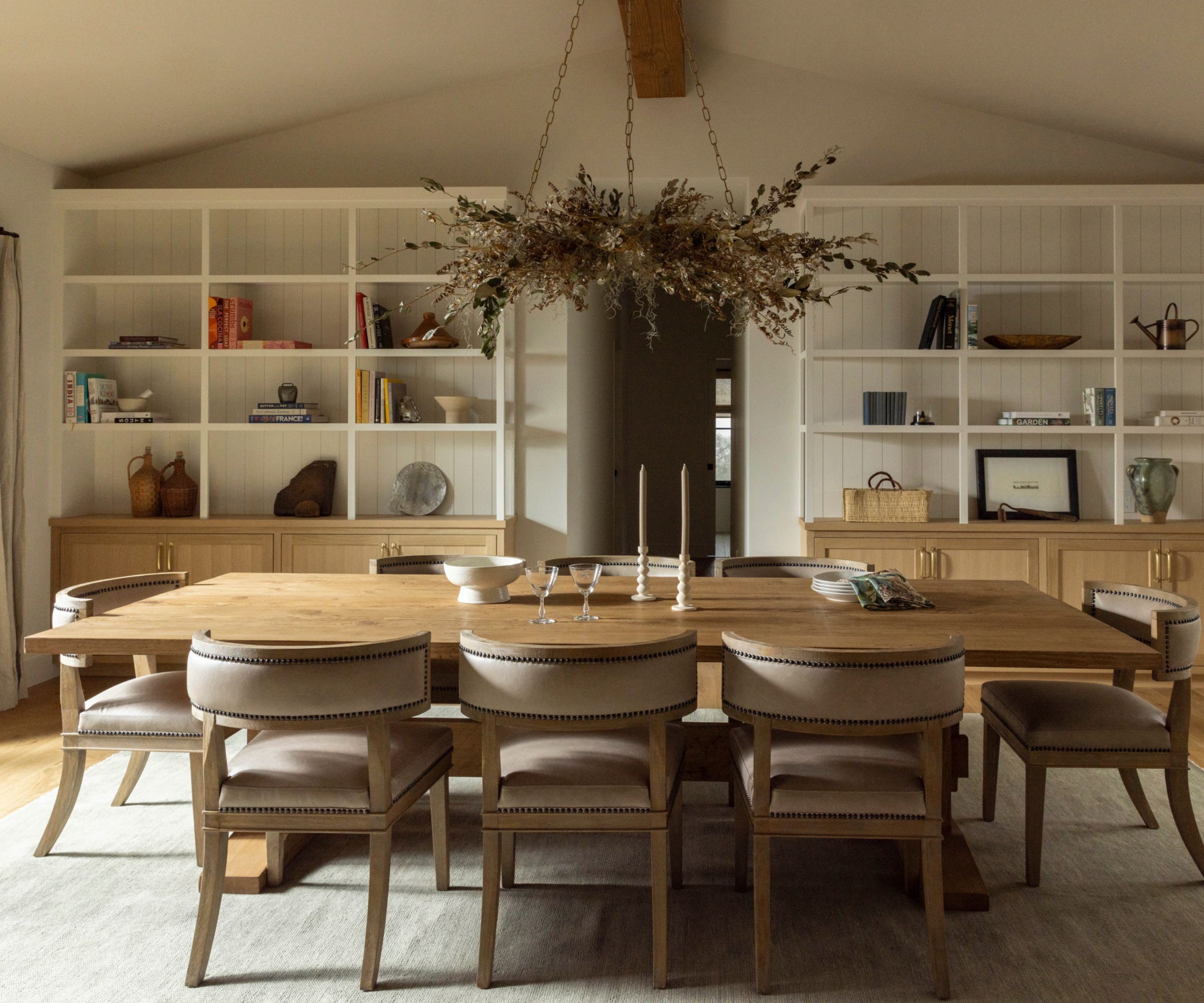 warm minimalist wooden dining room with large oak table and chairs, statement chandelier and white open shelving