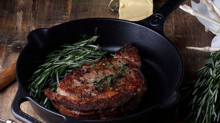 A black cast iron skillet on a wooden worktop with a fried steak inside. 