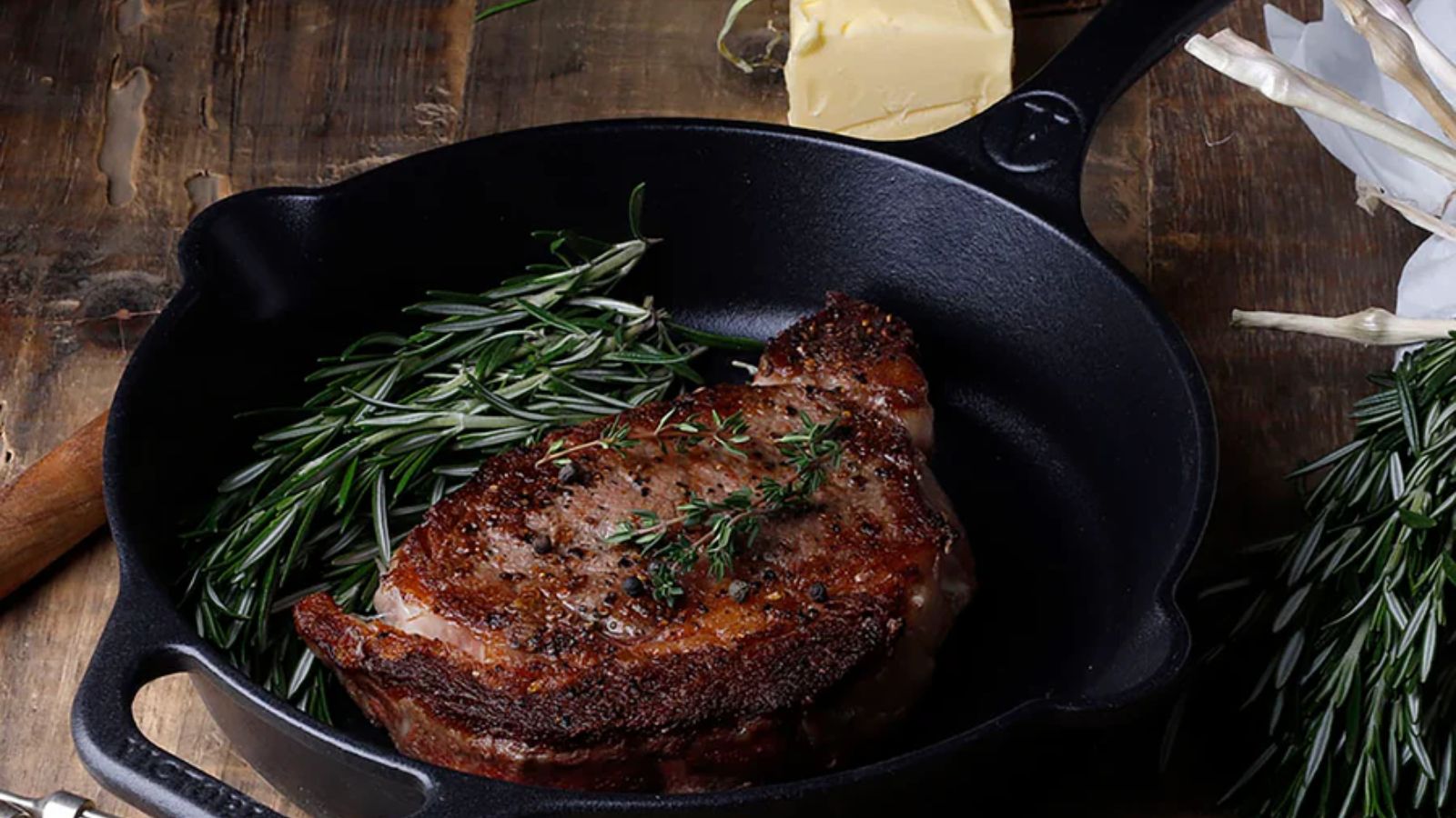A black cast iron skillet on a wooden worktop with a fried steak inside. 