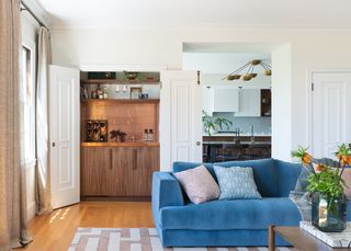 White living room with a hidden bar corner that has a copper backsplash. There is a blue velvet couch