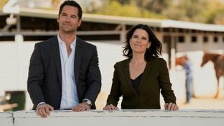Manuel Garcia-Rulfo and Neve Campbell as Mickey and Maggie smiling at horsing grounds in The Lincoln Lawyer season 2 episode 3