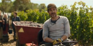 Amat (Santiago Cabrera) sits in a tractor in the middle of a vineyard, with a trailer full of grapes behind him and various women in the distant background picking grapes