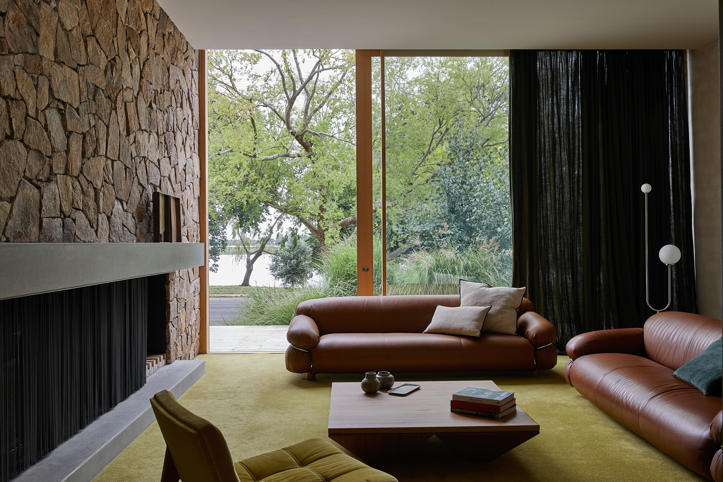A living room with green carpet with leather sofas, a rock wall, and large sliding doors