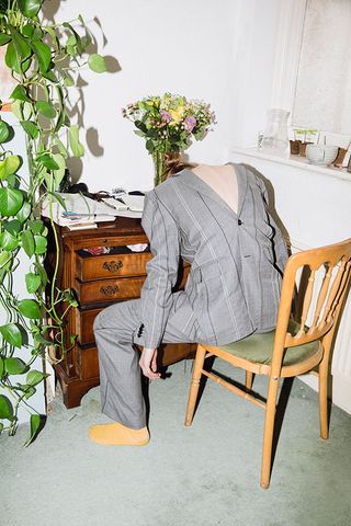 faceless model slouched over work desk wearing a grey suit back to front