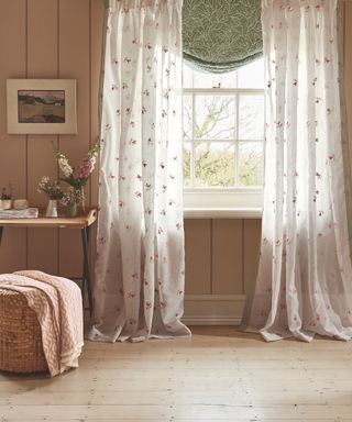 home office/bedroom with drapes and blind, shiplap walls painted in stone, footstool with throw, desk with flowers, artwork