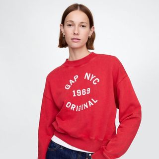 A woman wears a Gap red sweatshirt stood against a light background