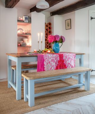 blue painted farmhouse style table and benches in a cottage dining area with pink table runner, flowers and candlelight