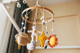 A baby's mobile hangs with plush planets, an astronaut and rocketship