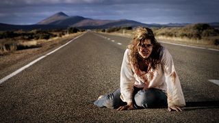 En kvinne i blodige klær på en vei i Australias outback i skrekkfilmen Wolf Creek.