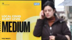 A woman walks in front of a sign displaying a tier two coronavirus warning