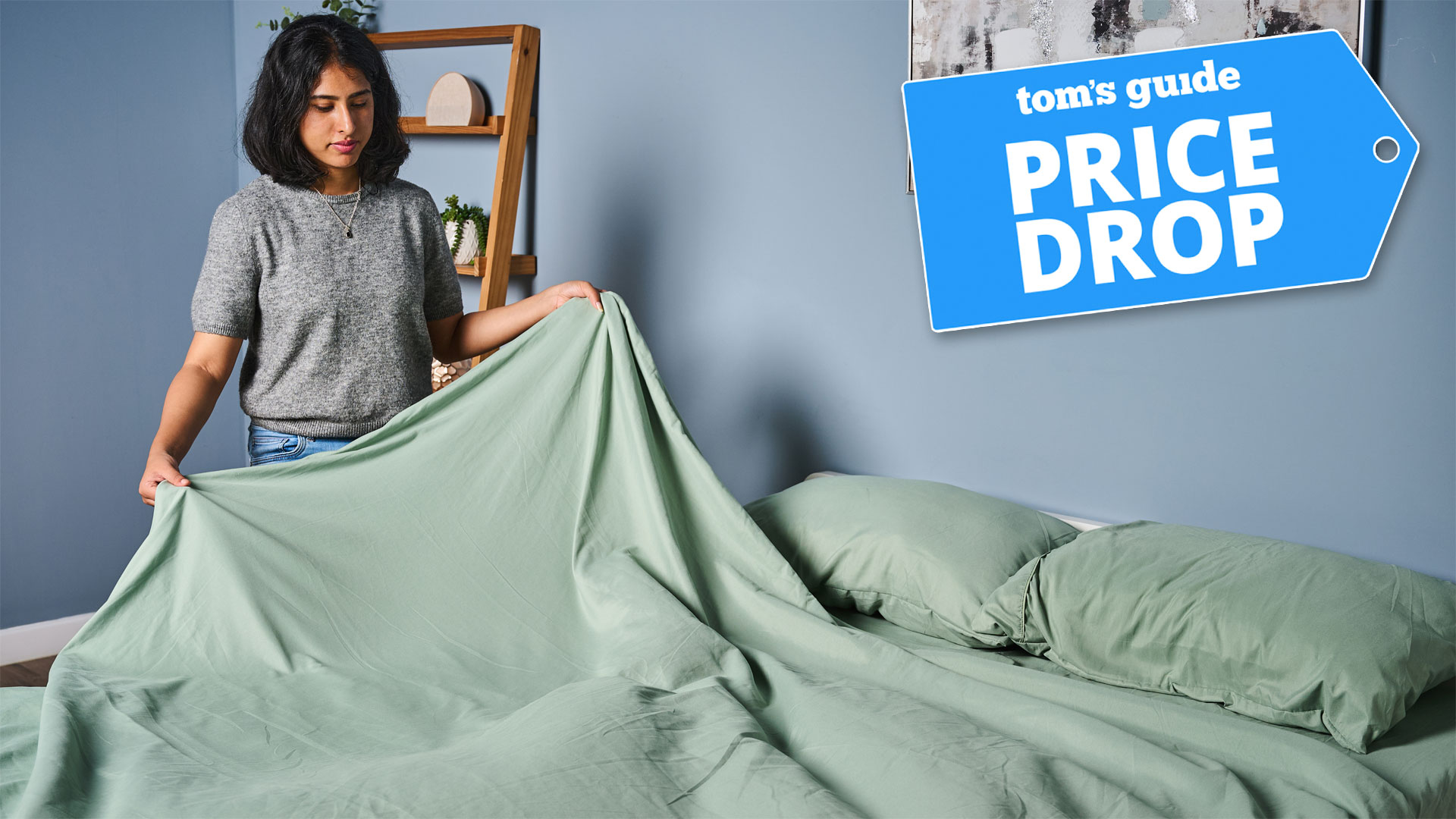 A woman fitting the Utopia Bedding Sheet Set on a bed, with a Tom's Guide badge overlaid saying &amp;quot;PRICE DROP&amp;quot;