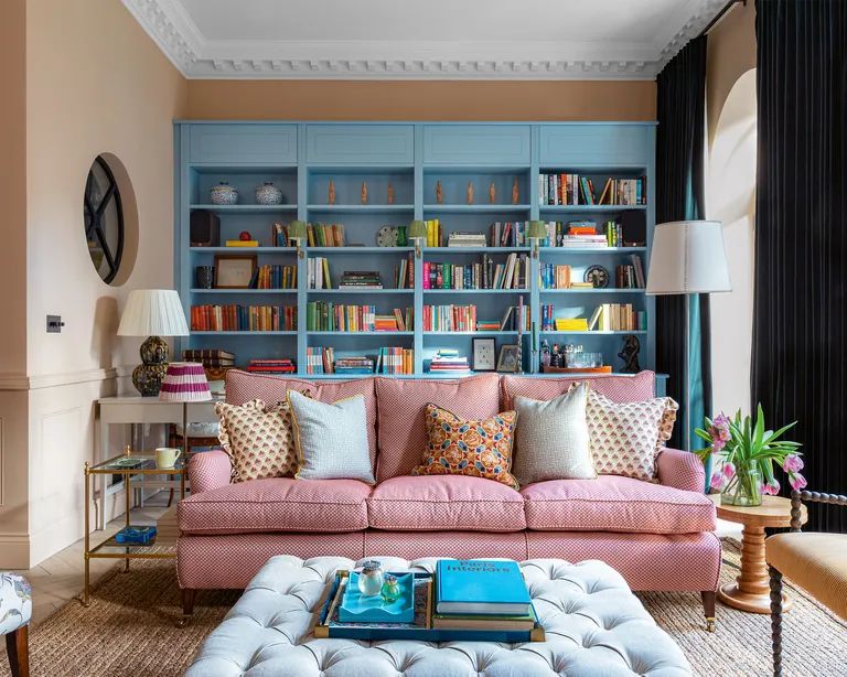 Colorful living room with bespoke blue shelving, red patterned sofa, ottoman, side tables,