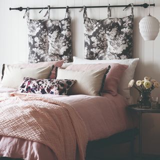 A bedroom with pink bedding bedding and floral cushions
