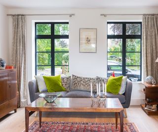 Living room with grey sofa with green cushions and coffee table in front of two long hertiage-style windows from Kloeber