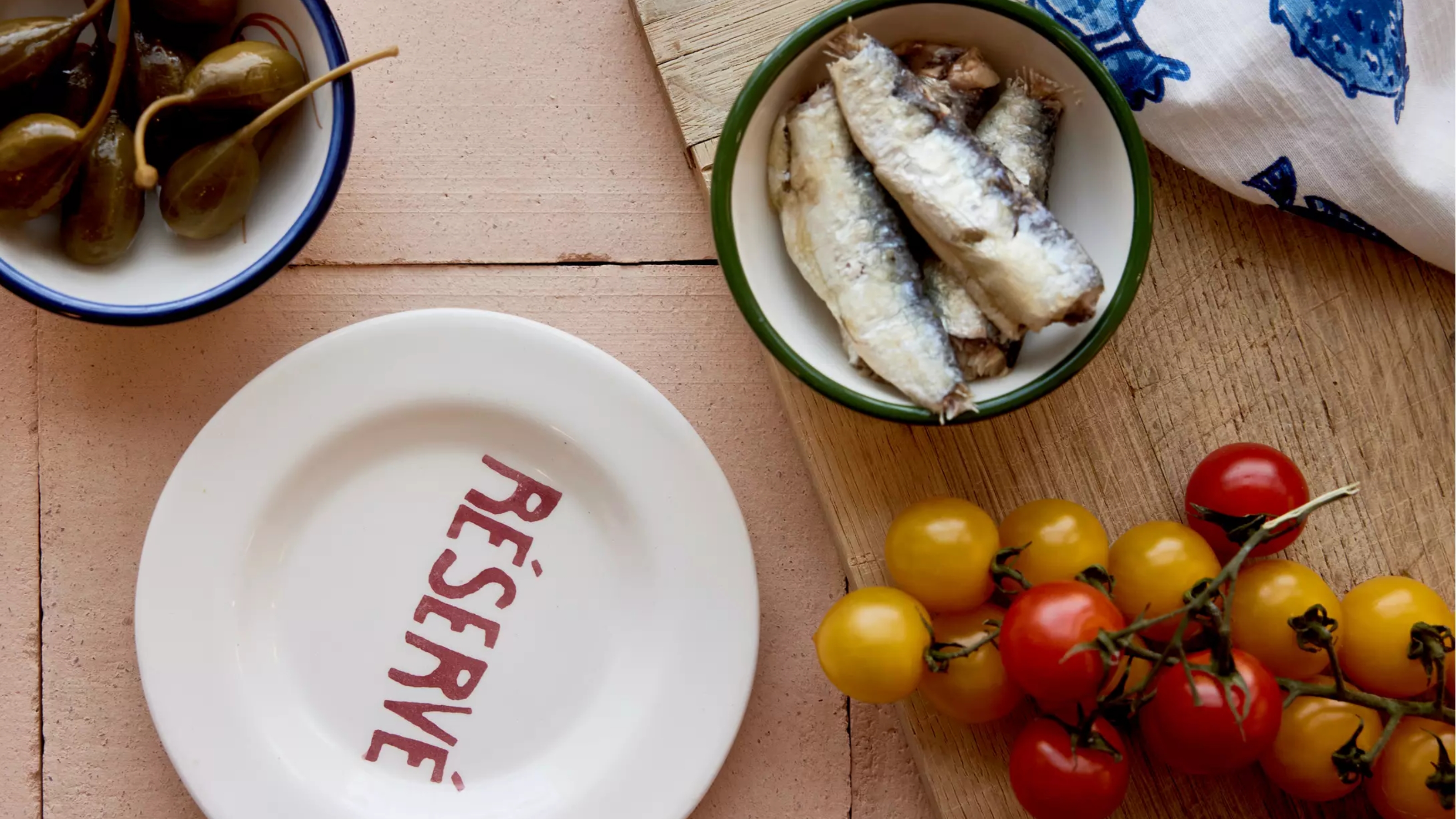 a plate with reserve written on next to some tomatoes, sardines and capers in a bowl