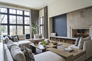 neutral living room with large sectional, log pile, coffee table, drapes, black crittal windows, stone fireplace