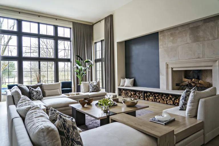 neutral living room with large sectional, log pile, coffee table, drapes, black crittal windows, stone fireplace