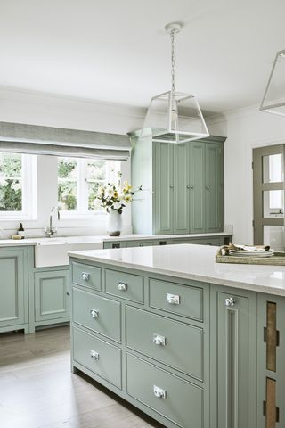 Kitchen with green cabinets, island with pendant lights, wood floor and white walls