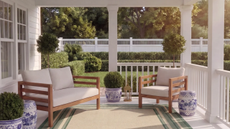 a porch with a loveseat and an accent chair, a green-bordered rug, and chinoiserie side tables and pots 
