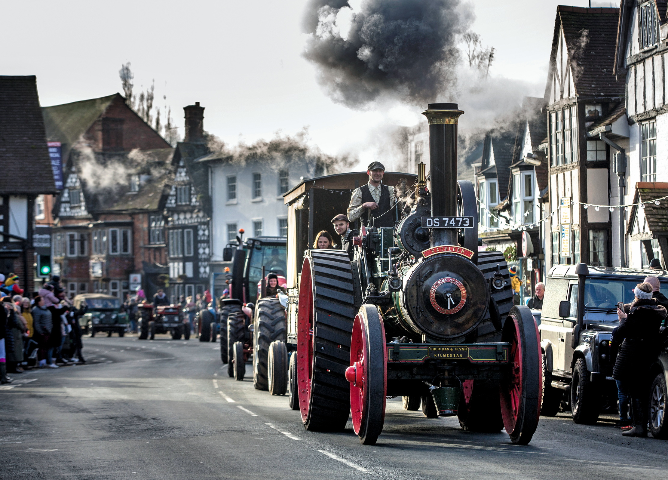 A traction engine leads a parade through a village