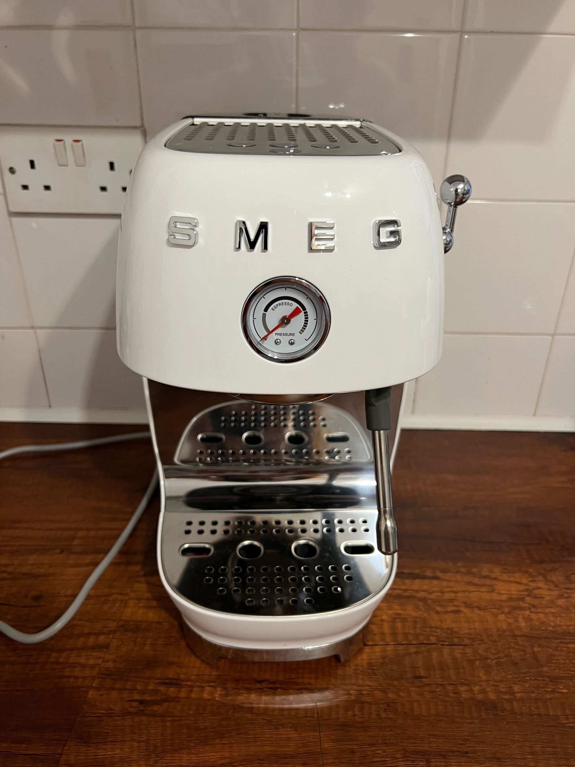 Image of a white Smeg cold brew machine on a wooden countertop with white tile backsplash