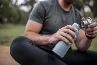 A man holding a grey, reusable water bottle in his hands with the lid off.
