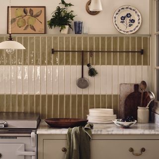 olive and cream tiled splashback, white AGA, stone cabinets with marble worktop, wooden bowls, hanging rail, artwork, wall light, tableware