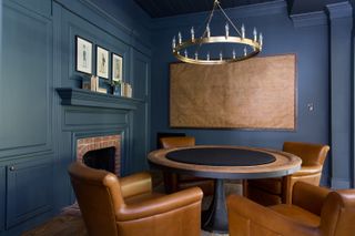 Dark blue dining space with large circular table and brown leather chairs