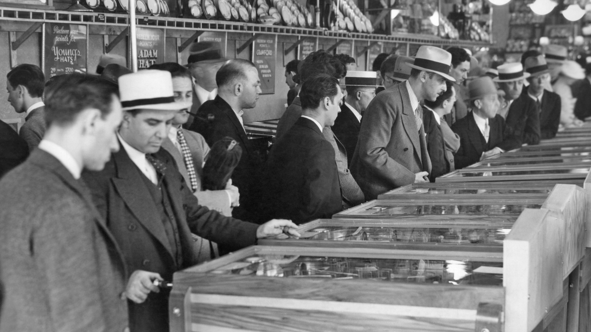 1930s GROUP MEN WEARING HATS PLAYING MARBLE PINBALL MACHINES IN BROADWAY AMUSEMENT ARCADE TIMES SQUARE NEW YORK CITY USA (Photo by Charles Phelps Cushing/ClassicStock/Getty Images)
