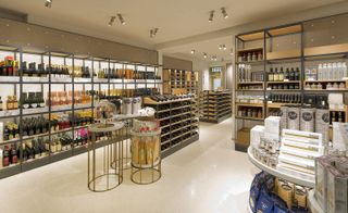 A store floor featuring white ceiling with ceiling lights, white floors and shelved walls with gourmet selections on display.