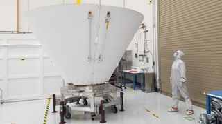 a technician in a white clean suit looks up at a large white cone-shaped device