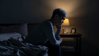 Man sat on the edge of his bed, resting his head in his hands, after waking up early