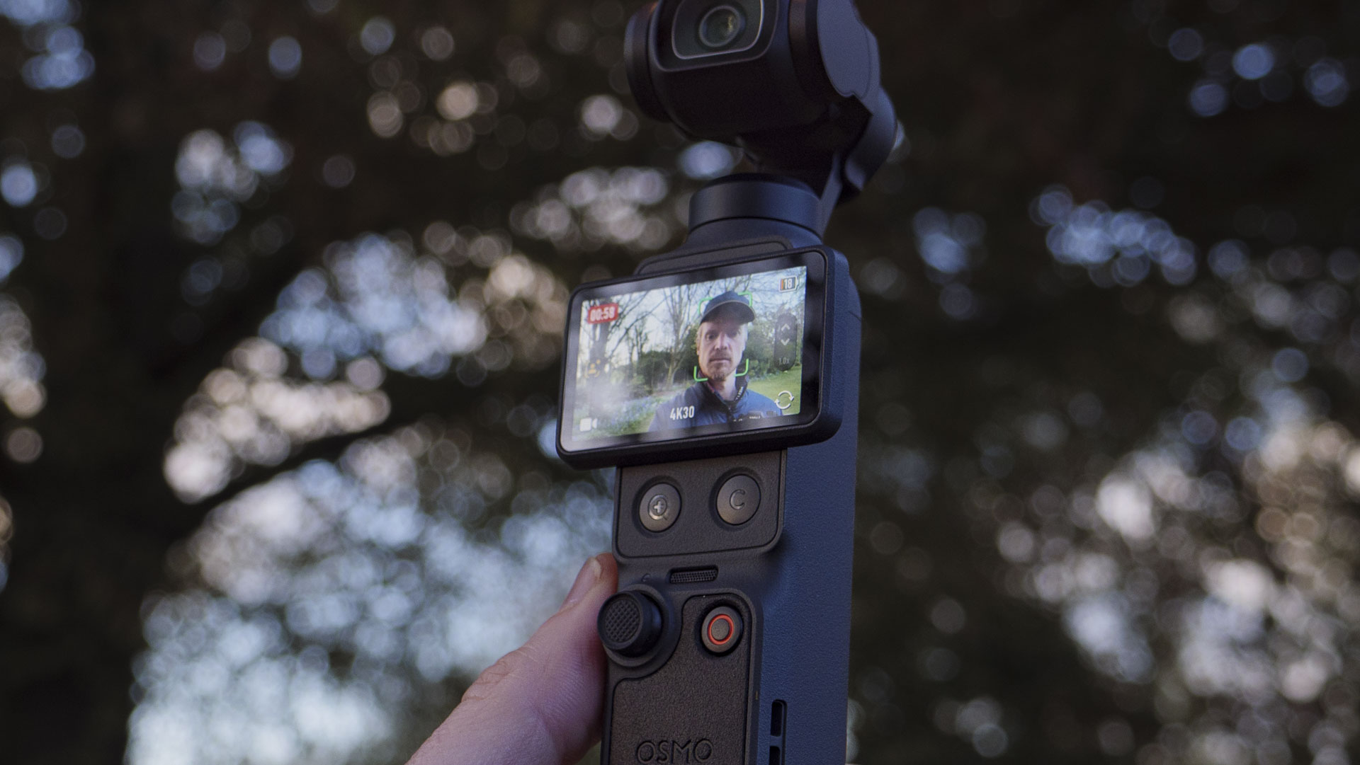 DJI Osmo Pocket 4 vlogging camera with natural background at golden hour, and the user in the frame of the screen