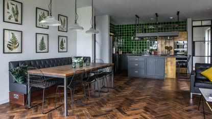 A Victorian. industrial style kitchen with white walls, black dining bench, black cabinetry and green glazed tiles 