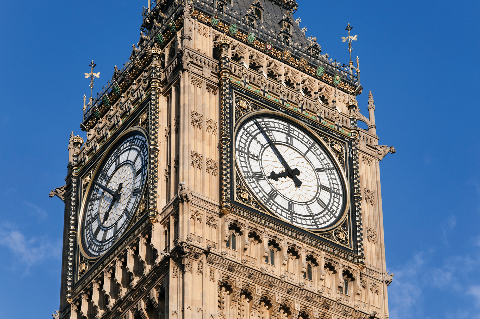 Close-up of Big Ben's clock face against a clear blue sky, showcasing intricate designs and golden accents on the iconic tower