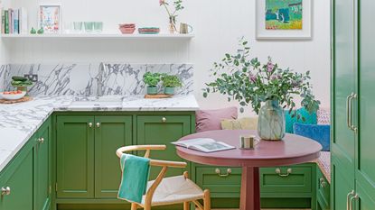 small green kitchen with marble splashback and banquette seating area and painting on wall