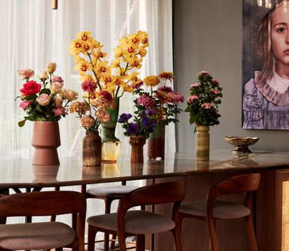 A selection of flowers in six different vases on a wooden dining room table