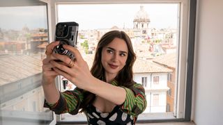 Emily takes a selfie in front of her apartment window in Rome in Emily in Paris