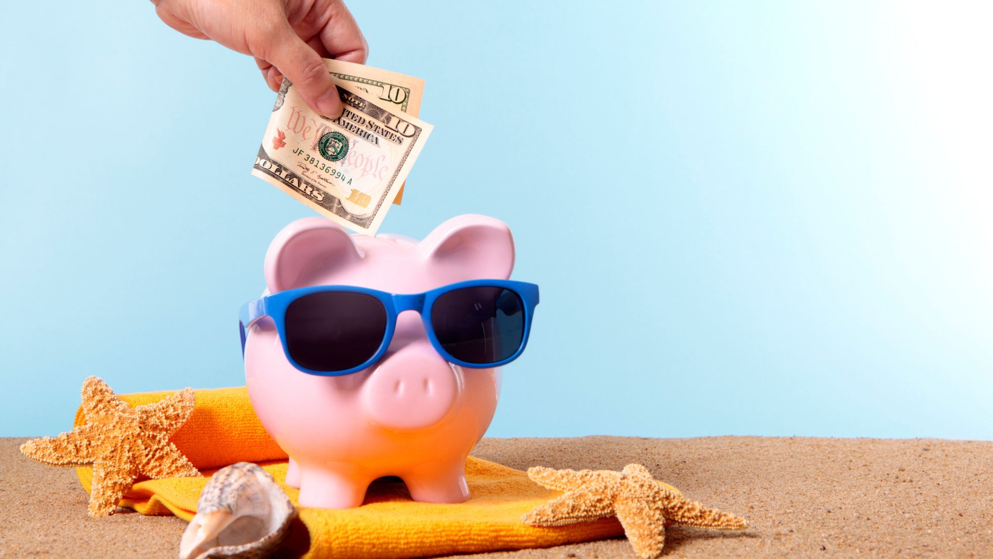 Pink piggy bank with beach items and money being put in 